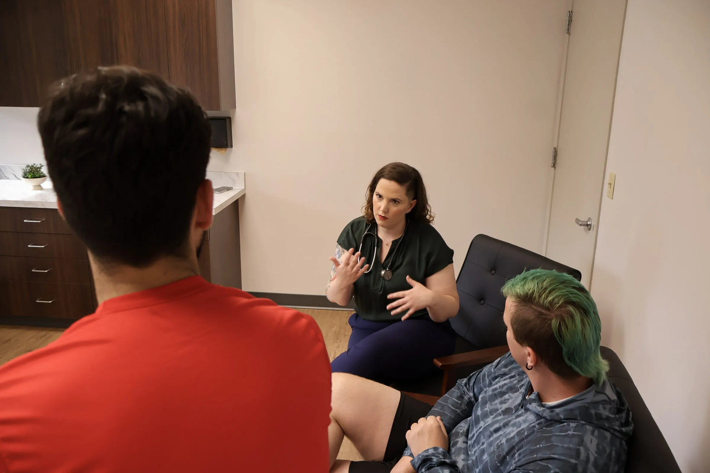 Dr. Oropeza talking with two patients in an exam room, leaning forward mid-conversation.