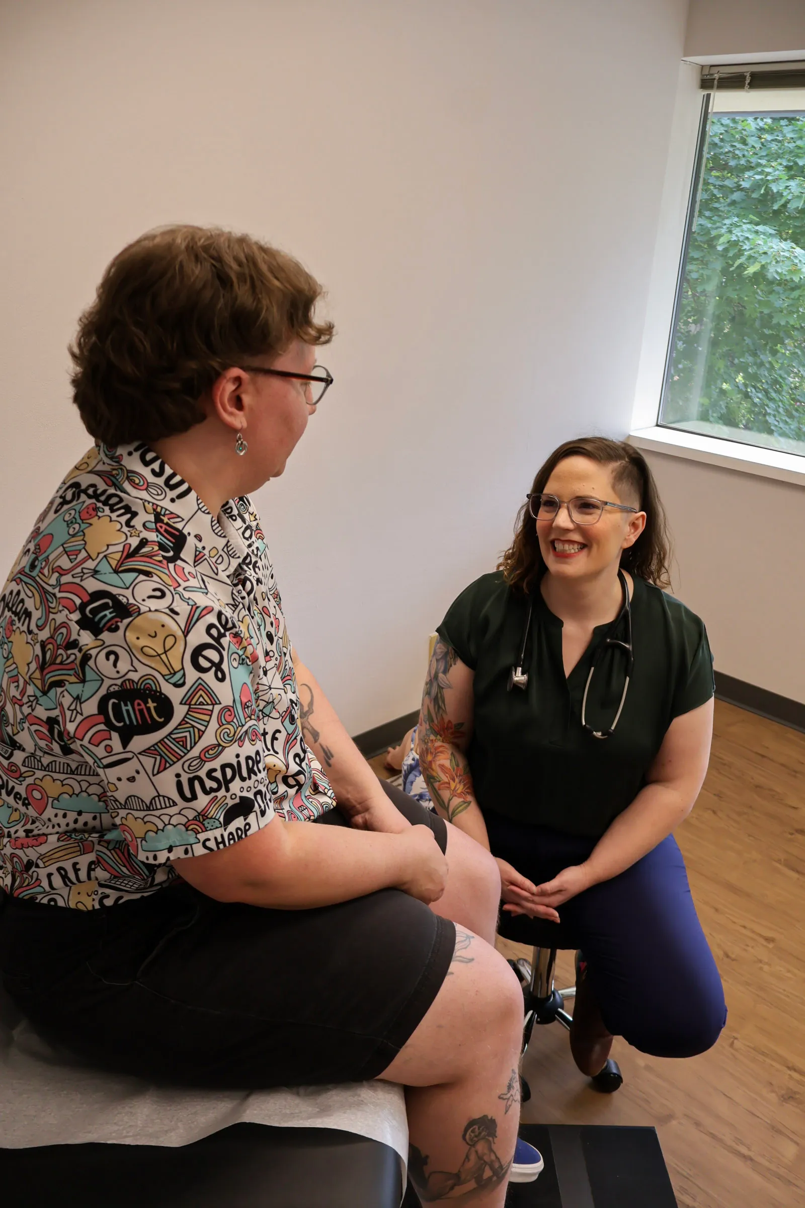 Dr. Oropeza smiles with a patient in a sunlit exam room as they talk face to face.